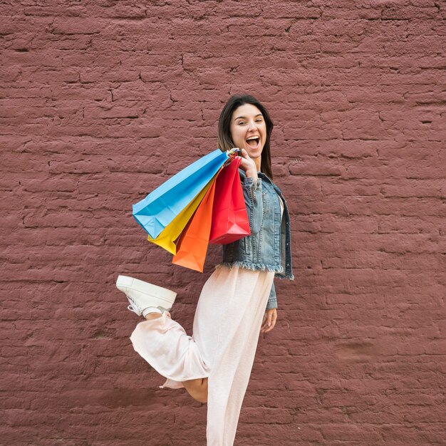 Foto gratuita joven dama con muchas bolsas de compras brillantes cerca de pared de ladrillo