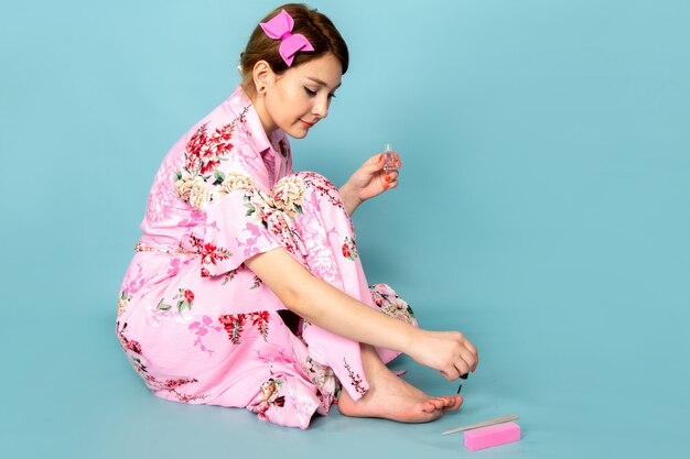 Foto gratuita una joven dama de vista frontal en vestido rosa diseñado con flores pintando sus uñas en azul