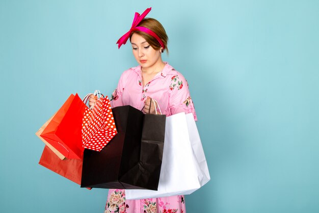 Una joven dama de vista frontal en vestido rosa diseñado con flores sosteniendo paquetes de compras en azul