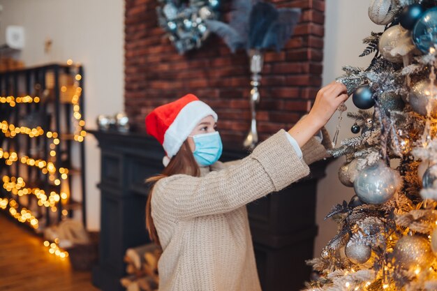 Una joven decora el árbol de Navidad con máscaras médicas.