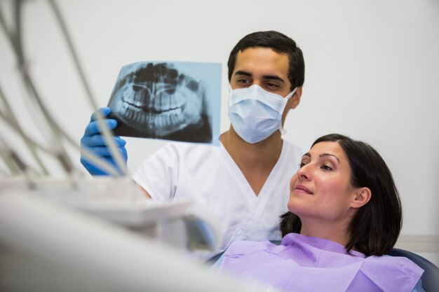 Joven dentista masculino que examina la radiografía con la paciente