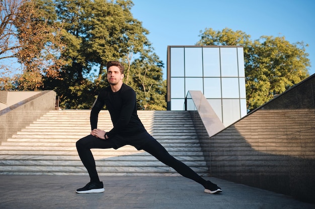 Foto gratuita joven deportista atractivo que se extiende durante el entrenamiento matutino en el parque de la ciudad