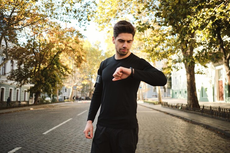 Foto gratuito joven deportista atractivo revisando cuidadosamente su reloj después de correr por la mañana en la calle de la ciudad