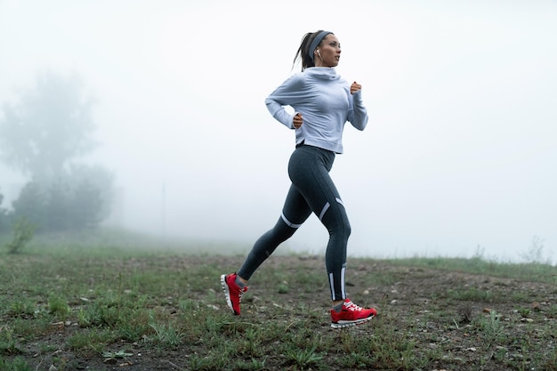 Foto gratuita joven deportista corriendo a lo largo de un campo de niebla en la naturaleza copiar espacio