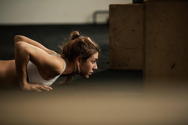 Joven deportista dedicada ejerciendo flexiones durante el entrenamiento deportivo en el club de salud Copiar espacio