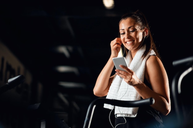 Joven deportista feliz usando teléfono móvil y escuchando música mientras hace ejercicio en el gimnasio Copiar espacio