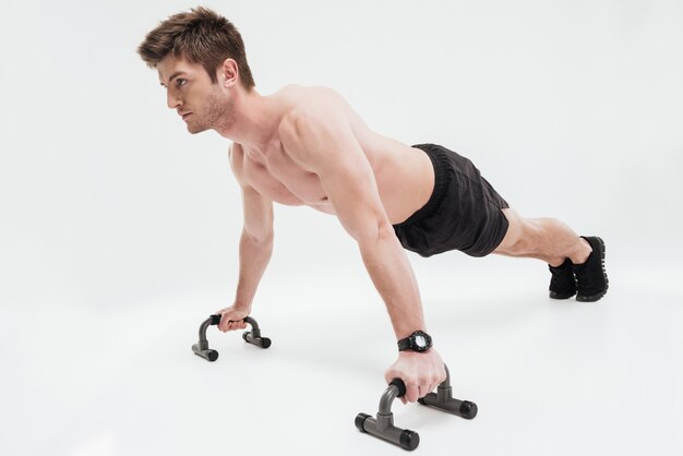 Joven deportista en forma haciendo flexiones con barras