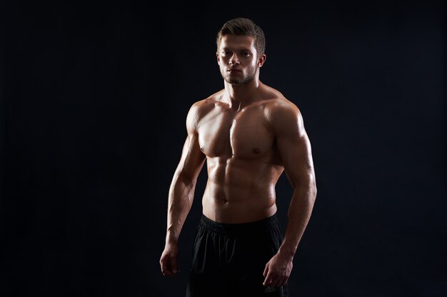 Joven deportista en forma muscular posando sin camisa sobre fondo negro