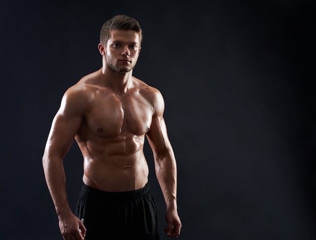 Joven deportista en forma muscular posando sin camisa sobre fondo negro