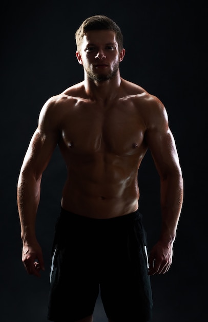 Joven deportista en forma muscular posando sin camisa sobre fondo negro