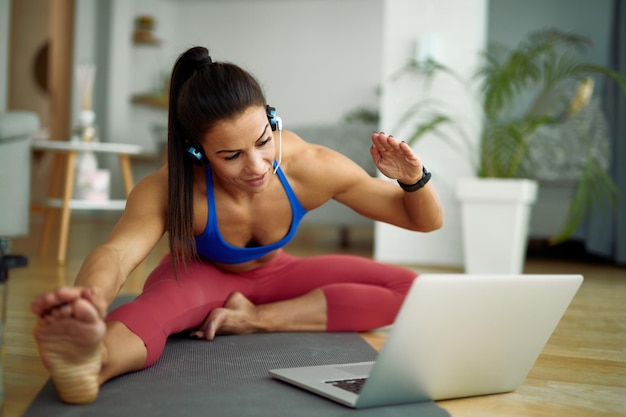 Joven deportista haciendo ejercicio en el suelo mientras sigue una clase de ejercicio en línea con una laptop en casa