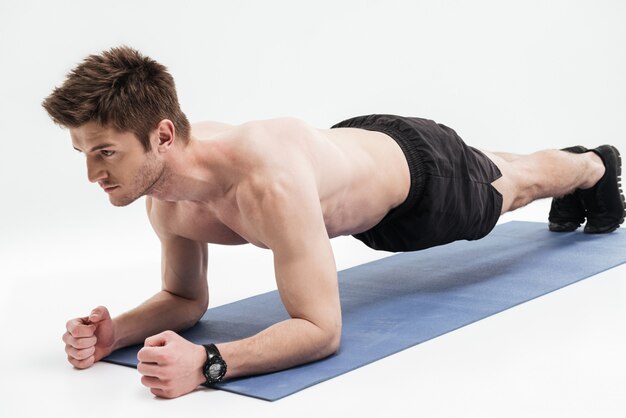 Joven deportista haciendo ejercicio de tabla sobre una estera de fitness