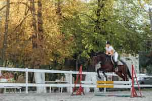 Foto gratuita joven deportista de jinete de caballo en la competición de deporte ecuestre saltando por encima del obstáculo