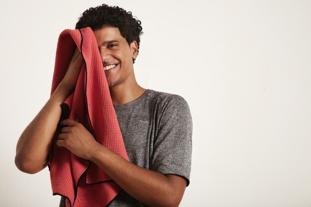 Joven deportista negro se ríe y se limpia la cara con una toalla roja, la mitad derecha de la cara abierta en blanco