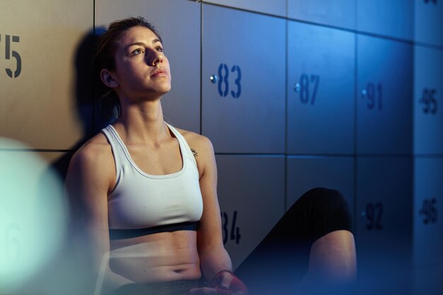 Joven deportista pensando mientras está sentada en el vestuario del gimnasio y preparándose para el entrenamiento deportivo