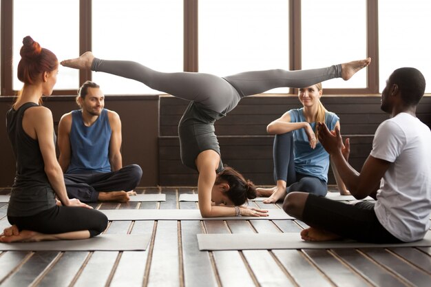 Joven deportista en pose de Pincha Mayurasana y un grupo.