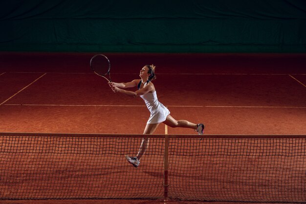 Joven deportista profesional caucásica jugando al tenis en la cancha deportiva. Entrenando, practicando en movimiento, acción. Poder y energía. Movimiento, publicidad, deporte, concepto de estilo de vida saludable. Angulo alto.