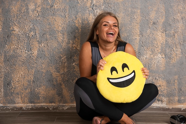 Foto gratuita joven deportista en ropa deportiva sosteniendo una almohada emoji sonriente debajo.