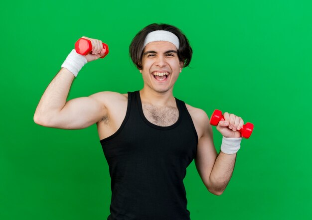 Joven deportista vistiendo ropa deportiva y diadema trabajando con pesas sonriendo alegremente