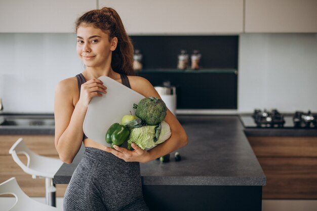 Joven deportiva con escalas y verduras en la cocina