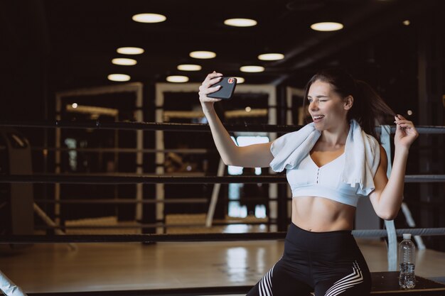 Joven deportiva tomando un selfie con teléfono móvil en el gimnasio.