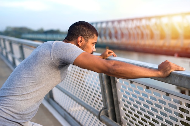 Joven deportivo concentrado para la formación Atleta concentrado mirando el río en la puesta del sol. Deportista preparándose para correr. Fitness y estilo de vida saludable.