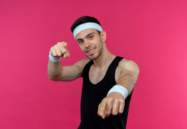 Foto gratuita joven deportivo en diadema apuntando con los dedos índices a la cámara sonriendo confiado sobre rosa