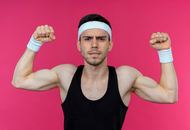 Joven deportivo en diadema mirando tenso levantando puño posando como atleta sobre rosa