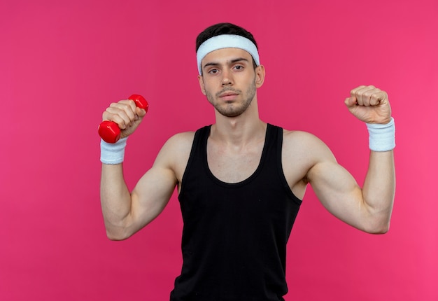 Foto gratuita joven deportivo en diadema trabajando con mancuernas tensas y confiadas sobre rosa