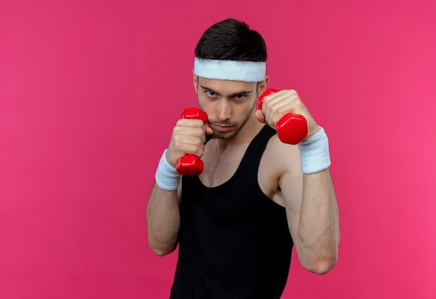 Foto gratuita joven deportivo en diadema trabajando con pesas tensas y confiado sobre rosa