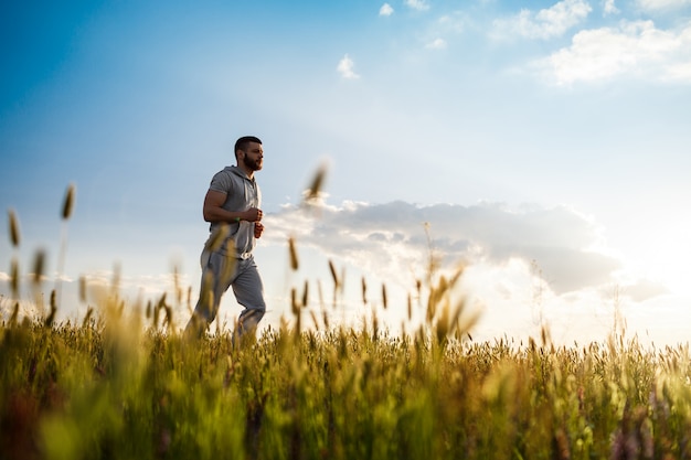 Joven deportivo trotar en el campo al amanecer.