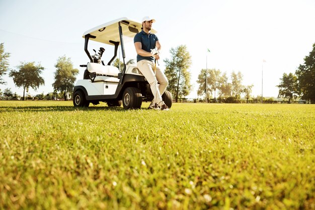 Joven descansando mientras se apoya en un carrito de golf