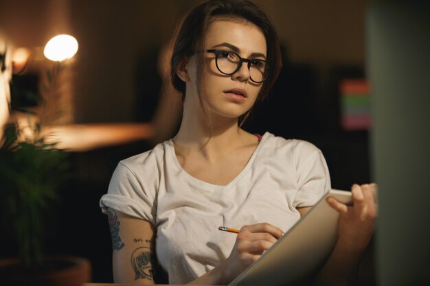 Joven diseñadora concentrada escribiendo notas usando la computadora