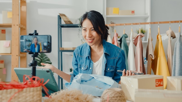 Joven diseñadora de moda asiática que usa el teléfono móvil que recibe la orden de compra y muestra la ropa en transmisión en vivo