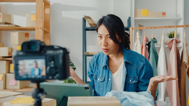 Joven diseñadora de moda asiática que usa el teléfono móvil que recibe la orden de compra y muestra la ropa en transmisión en vivo