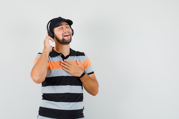 Foto gratuita joven disfrutando de la música con auriculares en camiseta, gorra y aspecto lindo. vista frontal.