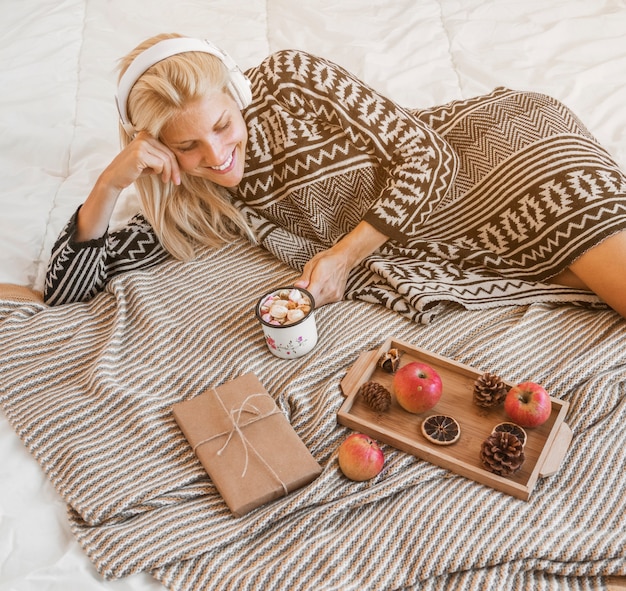 Foto gratuita joven disfrutando de la música y la bebida caliente en la cama