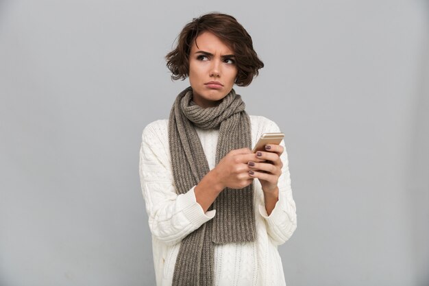 Joven disgustada con bufanda chateando por teléfono móvil.