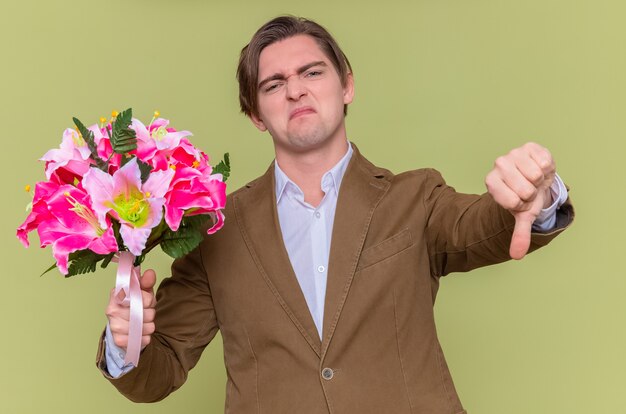 Joven disgustado sosteniendo ramo de flores mostrando el pulgar hacia abajo