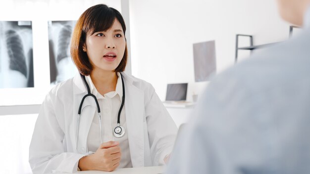 Joven doctora de Asia en uniforme médico blanco usando computadora portátil está brindando excelentes noticias, discuta los resultados