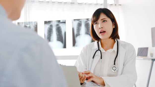 Joven doctora de Asia en uniforme médico blanco usando computadora portátil está brindando excelentes noticias, discuta los resultados