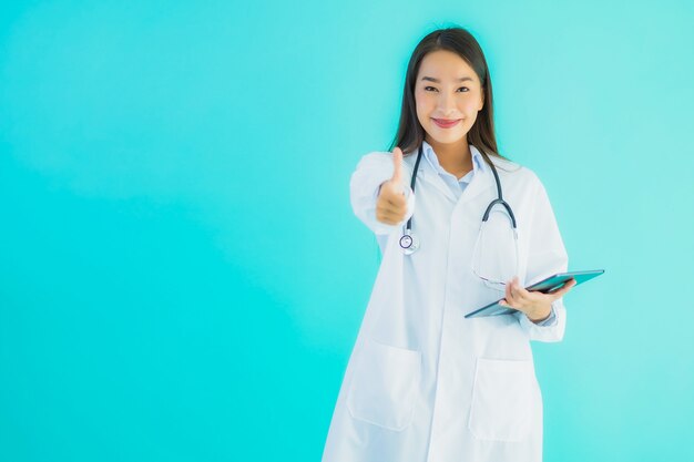 Joven doctora asiática con estetoscopio y tableta mostrando el pulgar hacia arriba