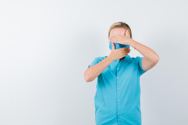 Joven doctora cubriendo los ojos y la boca con las manos en uniforme y mirando confiado aislado