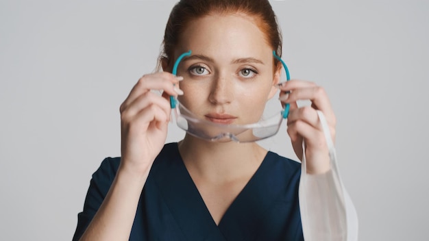 Joven doctora mirando atentamente a la cámara con anteojos protectores sobre fondo blanco El primer concepto de seguridad