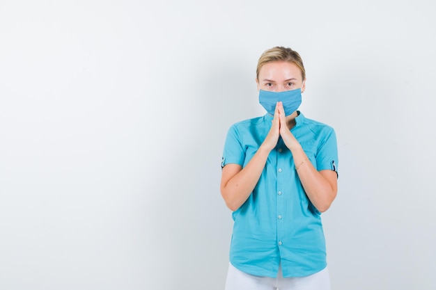 Joven doctora mostrando las manos juntas en gesto de súplica en uniforme