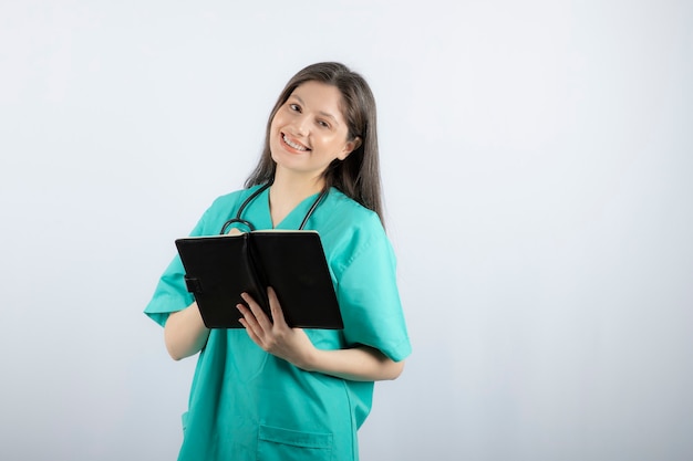 joven doctora de pie con cuaderno y lápiz.