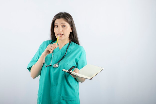 joven doctora de pie con cuaderno y lápiz.