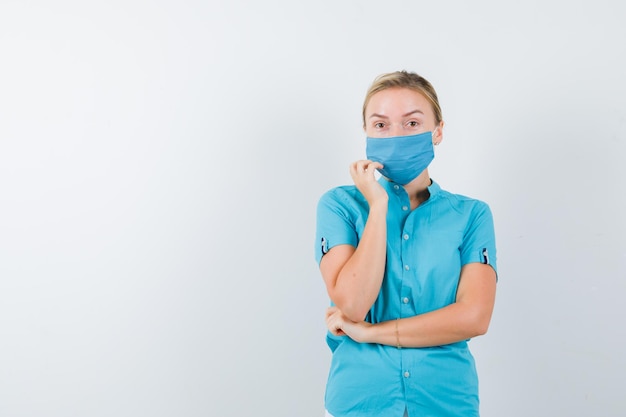 Joven doctora de pie en pose de pensamiento en uniforme y mirando vacilante aislado