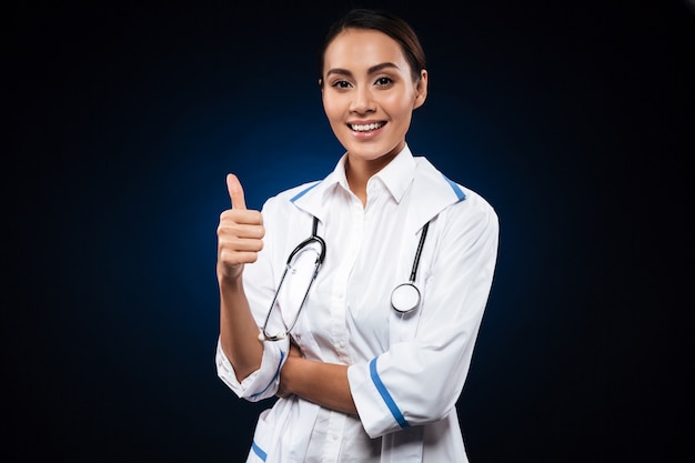 Joven doctora positiva con estetoscopio mostrando el pulgar hacia arriba