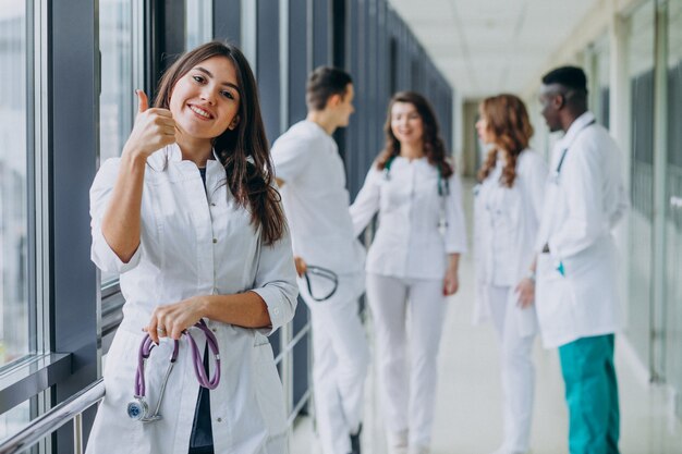 Joven doctora con pulgares arriba gesto, de pie en el pasillo del hospital